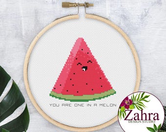 May include: A cross-stitch pattern in a round wooden embroidery hoop featuring a pink watermelon slice with a smiling face and black seeds. The text below the watermelon reads, "YOU ARE ONE IN A MELON" in black, capitalized, sans-serif letters.
