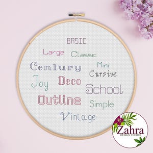 Könnte beinhalten: Ein runder Stickrahmen aus Holz mit weißem Aida-Stoff, auf dem verschiedene Wörter in unterschiedlich farbigen Garnen und Schriftarten gestickt sind, darunter Basic, Large, Classic, Century, Mini, Cursive, Joy, Deco, School, Outline, Simple und Vintage.