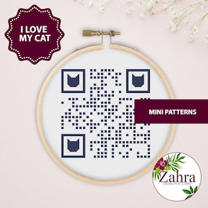 Pode incluir: Um aro de bordado branco com um padrão de código QR azul e branco com tema de gato. O aro está sobre um fundo rosa com flores brancas. O texto "I LOVE MY CAT" está em um adesivo de estrela marrom. O texto "MINI PATTERNS" está em texto preto sobre um retângulo marrom. O texto "Zahra DESIGN STUDIO" está em texto branco sobre um círculo marrom.