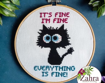 May include: A circular wooden embroidery hoop containing white fabric with a cross-stitch design of a black cat with large, wide, bloodshot blue eyes. The text reads IT'S FINE I'M FINE above the cat and EVERYTHING IS FINE! below the cat.