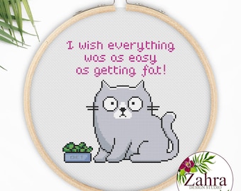 May include: A circular wooden embroidery hoop containing white fabric with a cross-stitch design of a gray cat sitting next to a blue bowl labeled DIET. The text above the cat reads I wish everything was as easy as getting fat! in pink.