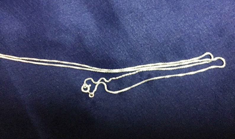 May include: A silver chain necklace with a delicate, box chain design. The chain is folded in half and appears to be new.