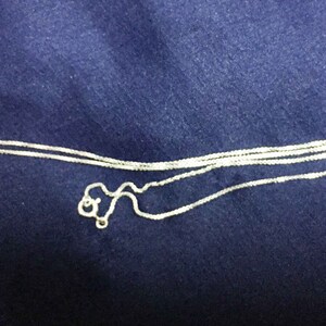 May include: A silver chain necklace with a delicate, box chain design. The chain is folded in half and appears to be new.
