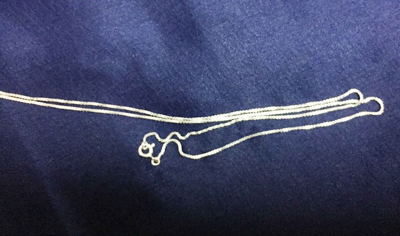 May include: A silver chain necklace with a delicate, box chain design. The chain is folded in half and appears to be new.