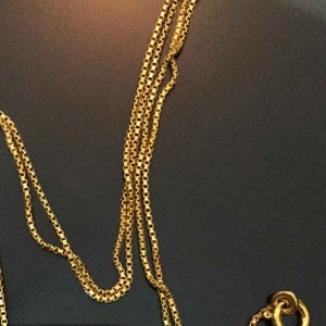 May include: A gold chain necklace with a box chain design. The chain is folded in half and the clasp is visible.