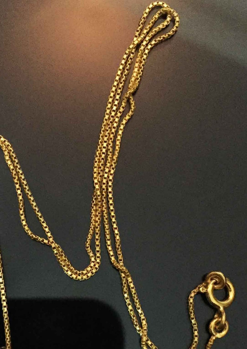May include: A gold chain necklace with a box chain design. The chain is folded in half and the clasp is visible.