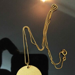 May include: A gold chain necklace with a round pendant. The chain is a box chain style.