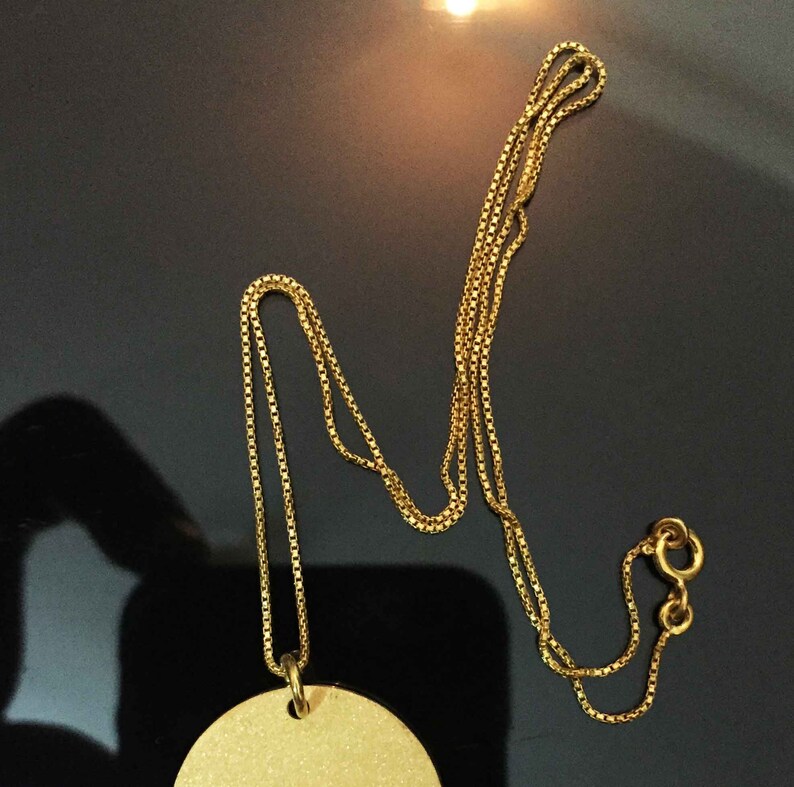 May include: A gold chain necklace with a round pendant. The chain is a box chain style.