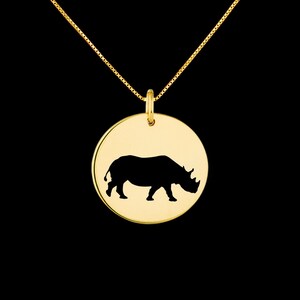 May include: Gold necklace with a round pendant featuring a black silhouette of a rhinoceros.