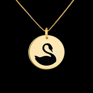 May include: A gold necklace with a round pendant featuring a black silhouette of a swan.