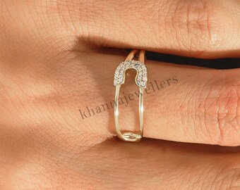 May include: A gold ring with a safety pin design, encrusted with small clear stones.