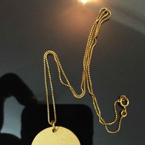 May include: A gold chain necklace with a round pendant. The chain is a box chain style.