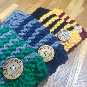 May include: Four knitted cup cozies in different color combinations, each with a wooden button featuring a dachshund and the text "The Silly Sausage".