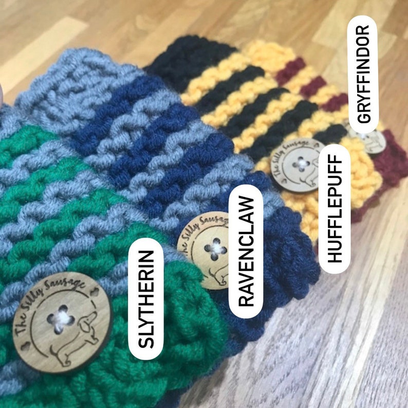 May include: Four knitted mug cozies in the colors of the Hogwarts houses: Gryffindor, Hufflepuff, Ravenclaw, and Slytherin. Each cozy has a wooden button with a dachshund logo and the words "The Silly Sausage".