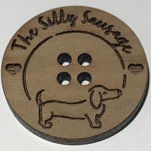 May include: A wooden button with four holes and a dachshund silhouette. The button is engraved with the text "The Silly Sausage".
