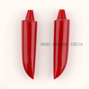 Puede incluir: Dos colgantes de coral rojo brillante en forma de diente. Los colgantes son lisos y pulidos, con una punta puntiaguda y una base redondeada.