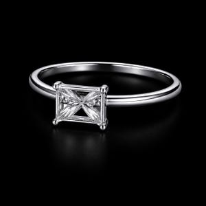 May include: A silver ring with a square-cut, clear gemstone. The ring band is thin and polished, and the gemstone is set in a square setting with four prongs. The background is black, highlighting the ring's details.