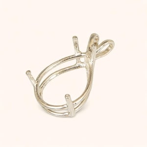 May include: A silver pendant setting in a teardrop shape. It has three prongs and a loop for a chain. The design is layered and open, designed to hold a gemstone or other decorative element. The setting is made of a silver-coloured metal.