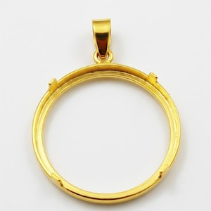 以下が含まれることがあります： 金色のペンダント。円形のフレームと、チェーンを通すための上部のループが付いています。ペンダントはシンプルでエレガントなデザインで、コインやその他の小さなアイテムを飾るのに最適です。ペンダントは光沢のある反射性の金属でできています。