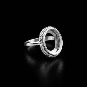 May include: A silver ring with an oval setting, featuring a textured rope-like design around the bezel. The ring's band is smooth and slender, and the setting is designed to hold a gemstone or other decorative element.