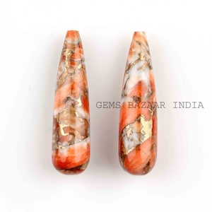 May include: Two teardrop-shaped pendants made of orange, white, and gold marbled stone.  The stone has a swirling pattern and is polished to a smooth finish.  GEMS BAZAAR INDIA is printed on the background.