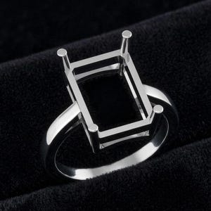 May include: A polished silver ring with a rectangular setting, designed for a gemstone. The ring has a classic design and a bright finish. The setting has four prongs to hold the stone. The ring is shown against a black background.