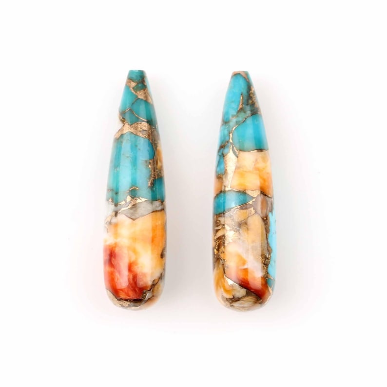 May include: Two teardrop-shaped turquoise stones with gold and red accents. The stones are polished and have a smooth surface.