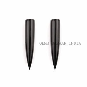 May include: Two black, pointed, horn-shaped objects.  The objects are smooth and shiny.  GEMS BAZAAR INDIA is printed in white letters on a black background.