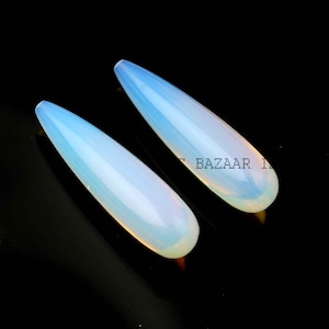 May include: Two teardrop-shaped, white opal beads. The beads are smooth and have a translucent, milky white color.