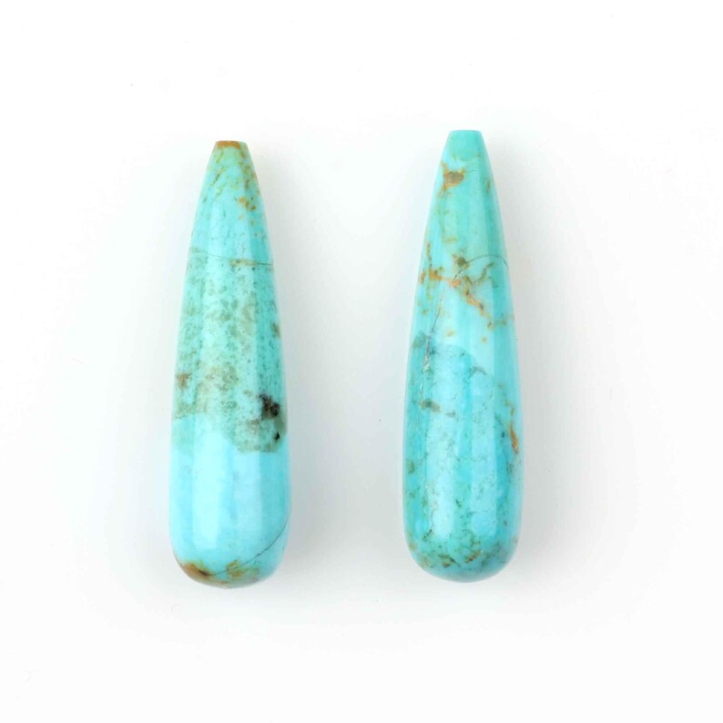 May include: Two teardrop-shaped turquoise stones with a light blue color and brown marbling.