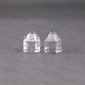 May include: Two clear quartz crystal points with a faceted, geometric design. The crystals are transparent and sit on a gray surface. The crystals are likely used for healing or decorative purposes.