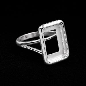 May include: A polished sterling silver ring featuring a rectangular bezel setting designed for a stone. The band is split into two thin arms that connect to the frame. The interior of the band is clearly stamped with the hallmark 925 for purity.