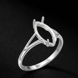 May include: A silver ring with a marquise-shaped setting, designed to hold a gemstone. The ring features a sleek, polished band and prongs to secure the stone. The ring is shown against a dark background.