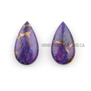 Könnte beinhalten: Zwei tropfenförmige Cabochons in Lila und Gold mit einem marmorierten Muster. Die Cabochons sind etwa 5 cm lang und 2,5 cm breit. Gems Bazaar India.