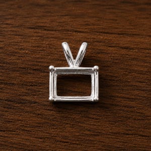 May include: A silver-toned rectangular pendant setting featuring four corner prongs designed to hold a gemstone. The metal frame has a smooth, polished finish and includes a V-shaped bail at the top for attachment to a chain or necklace.