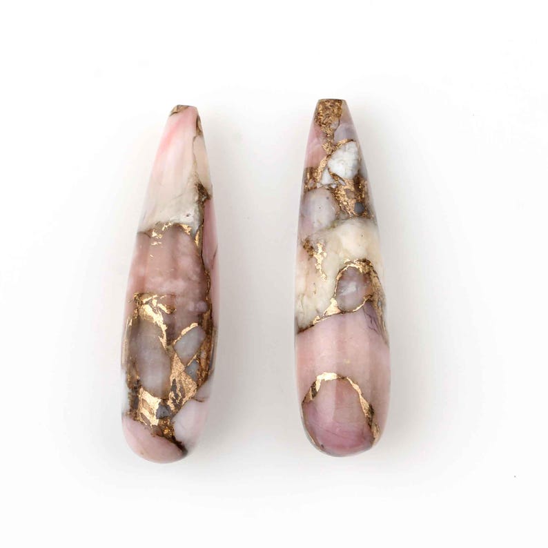 May include: Two teardrop-shaped pink and gold opal earrings. The earrings are made of a pink and white opal with gold flecks throughout.