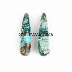 May include: Two teardrop-shaped turquoise and gold gemstone beads. The beads are a light blue and green color with gold flecks throughout.