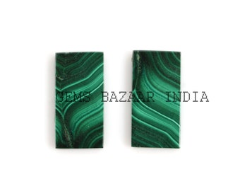 May include: Two rectangular pieces of malachite, a green gemstone, with a swirling pattern.  The pieces are approximately 2 inches long and 1 inch wide.  Gems Bazar India.