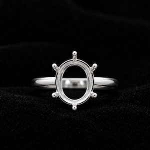 May include: A polished silver-toned ring setting featuring an oval-shaped head with six prongs extending outward. The band is smooth and rounded, designed to hold a single oval gemstone in a secure, elevated position above the finger.