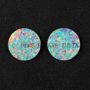 May include: Two round, iridescent opal cabochons with a white base and a variety of colors, including blue, green, pink, and yellow. The cabochons are approximately 1 inch in diameter. The text "Gems Bazaar India" is printed on the cabochons.