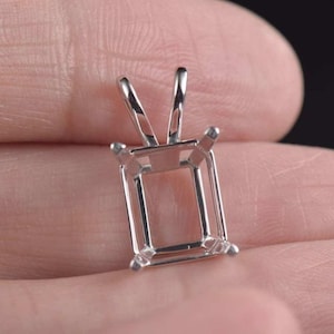 Peut inclure: Un support de pendentif argenté de forme rectangulaire, conçu pour contenir une pierre précieuse. Le support comporte quatre griffes aux coins et une boucle en haut pour une chaîne. Le métal est brillant et réfléchissant.