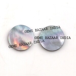 Puede incluir: Dos cabujones redondos de nácar iridiscente. Los cabujones tienen un diámetro de aproximadamente 2,5 cm y presentan una gama de colores gris, blanco y rosa. Los cabujones están etiquetados como "Gems Bazaar India".