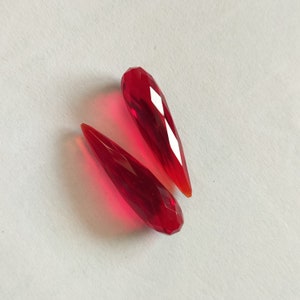 Peut inclure: Deux perles de cristal rouges en forme de larme avec des bords facetés.