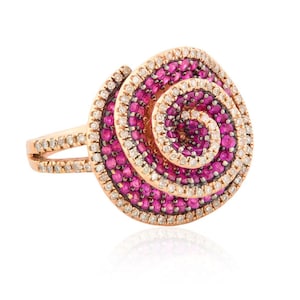 May include: Rose gold ring with a spiral design. The ring features a central swirl of pink gemstones, surrounded by a border of white gemstones. The band is split, with a row of white gemstones on each side. The ring is set against a white background.