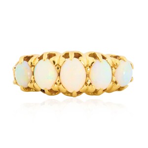 May include: A gold ring featuring five oval opals. The opals are set in a gold band with a textured design. The opals have a milky white color with subtle iridescent flashes.