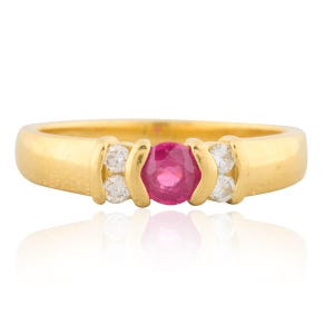 May include: A gold ring featuring a central oval ruby gemstone, flanked by two pairs of smaller, round, clear gemstones. The ring has a smooth, polished band and a classic design, suitable for everyday wear or special occasions.
