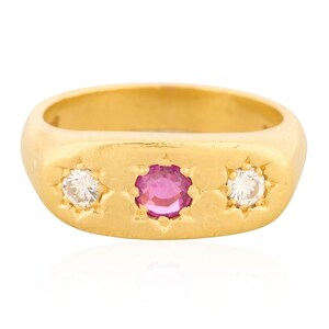 May include: A gold ring with a rectangular face, featuring a central pink gemstone flanked by two white gemstones. The gemstones are set within star-shaped designs, creating a classic and elegant look.