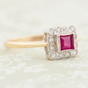 Op de afbeelding: Een gouden ring met een vierkante robijn omringd door een halo van kleine diamanten.