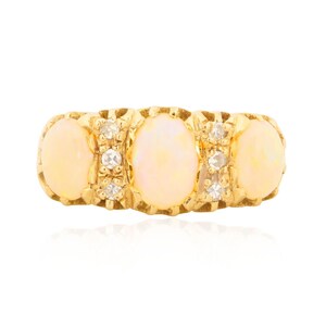 May include: A gold ring featuring three oval opals and small accent diamonds. The opals have a creamy, pale yellow color, and the ring's band has a textured, ornate design. The ring is a piece of jewelry.