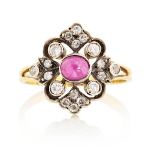 May include: A vintage-style ring featuring a central oval-cut pink gemstone, surrounded by a halo of small, sparkling diamonds. The ring has a gold band and a decorative, ornate setting, showcasing a classic and elegant design.